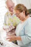 Senior Adult Couple Washing Dishes Together Inside Kitchen photo