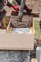 Construction Workers Pouring And Leveling Wet Cement Into Wood Framing photo