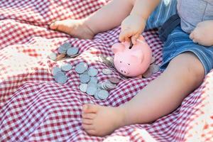 Baby Boy Sitting on Picnic Blanket PUtting Coins in Piggy Bank photo
