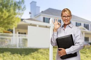 agente inmobiliario frente a una casa y un cartel en blanco foto