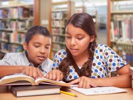 chico y chica hispanos divirtiéndose estudiando juntos en la biblioteca foto