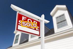 Left Facing Sold For Sale Real Estate Sign In Front of House and Deep Blue Sky. photo