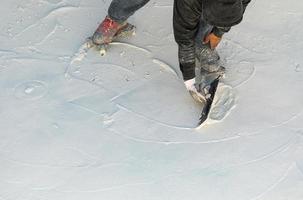 trabajador que usa zapatos con púas alisando el yeso húmedo de la piscina con una paleta foto