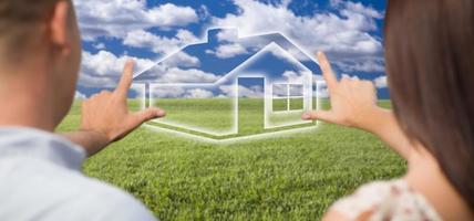 Couple Framing Hands Around House Figure in Grass Field photo