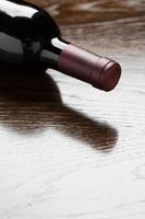 botella de vino tinto sobre una superficie de madera que se desvanece hasta el blanco.