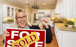 Young Woman Holding Sold Sign and Keys Inside New Kitchen photo