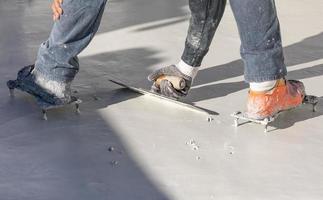 Worker Wearing Spiked Shoes Smoothing Wet Pool Plaster With Trowel photo