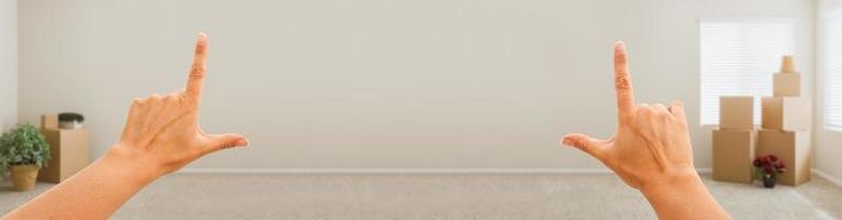 Female Hands Framing Blank Wall in Empty Room with Moving Boxes Banner. photo