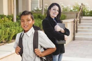 niño hispano con mochila en el campus de la escuela y profesor detrás foto