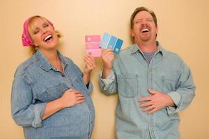 pareja embarazada que se ríe decidiendo sobre pintura de pared rosa o azul foto