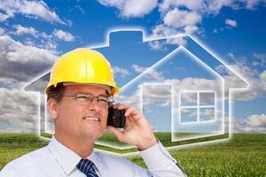 Contractor in Hardhat on Phone Over House, Grass and Clouds photo