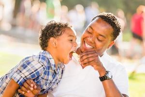 padre afroamericano e hijo de raza mixta comiendo una manzana en el parque foto