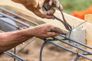 Trabajador que asegura la estructura de barras de refuerzo de acero con la herramienta de corte de alicates de alambre en el sitio de construcción foto