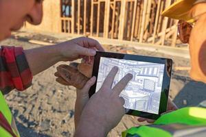 Male and Female Construction Workers Reviewing Kitchen Drawing on Computer Pad at Construction Site photo