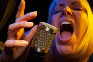 Female vocalist under gelled lighting sings with passion into condenser microphone. photo