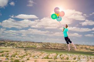 Young Girl Being Carried Up and Away By Balloons That She Is Holding Above The Town Below. photo