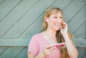 retrato al aire libre de una joven adulta de ojos marrones escuchando música con auriculares en su teléfono inteligente. foto