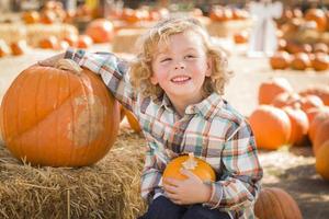 niño pequeño sentado y sosteniendo su calabaza en el huerto de calabazas foto