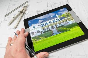 Hand of Architect on Computer Tablet Showing Home Photo Over House Plans