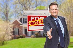Male Agent Reaching for Hand Shake in Front of House and Sold Real Estate Sign photo