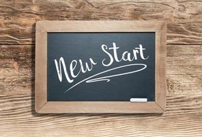 New Start Written on Slate Chalk Board Against Aged Wood Background photo