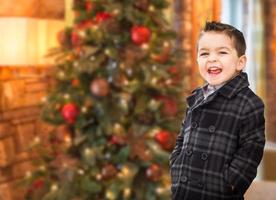 apuesto niño de raza mixta caucásico e hispano frente al árbol de navidad. foto