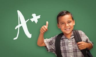 niño hispano con los pulgares hacia arriba frente a una pizarra escrita en tiza foto