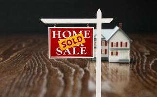 Sold For Sale Real Estate Sign In Front of Model Home on Reflective Wooden Surface. photo