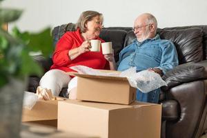 pareja adulta mayor cansada descansando en el sofá con tazas de café rodeadas de cajas móviles foto