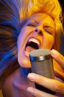 Female vocalist under gelled lighting sings with passion into condenser microphone. photo