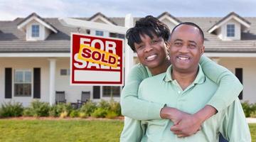 Happy African American Couple In Front of Beautiful House and Sold For Sale Real Estate Sign. photo