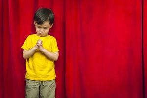 niño de raza mixta rezando frente a la cortina roja foto