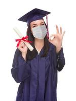 mujer graduada con mascarilla médica y toga y birrete aislada en un fondo blanco foto