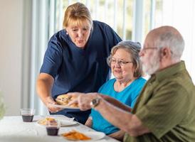 doctora o enfermera que sirve sándwiches para parejas de adultos mayores en la mesa foto