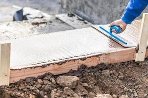 trabajador de la construcción usando paleta sobre cemento húmedo formando afrontamiento alrededor de la nueva piscina foto