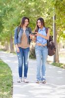 dos hermosas jóvenes hermanas gemelas étnicas con mochilas usando un teléfono inteligente afuera. foto