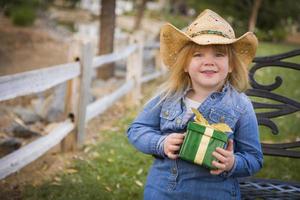 niña joven con ropa de vacaciones sosteniendo un regalo de navidad afuera foto