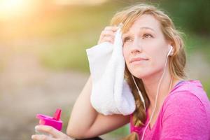 Young Fit Adult Woman Outdoors With Towel and Water Bottle in Workout Clothes Listening To Music with Earphones. photo