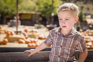 niño pequeño parado contra un viejo vagón de madera en un huerto de calabazas foto