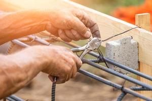 Worker Securing Steel Rebar Framing With Wire Plier Cutter Tool At Construction Site photo