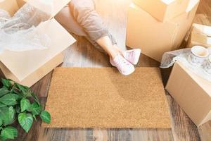 Woman Wearing Sweats Relaxing Near Home Sweet Home Welcome Mat, Moving Boxes and Plant photo