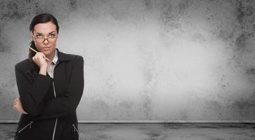 Young Adult Woman with Pencil and Glasses Standing In Front of Blank Grungy Blank Wall with Copy Space photo