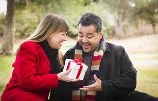 pareja de raza mixta compartiendo regalos de navidad o san valentín afuera foto