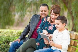 Caucasian Mother and Hispanic Father Using Computer Tablet With Mixed Race Son Outdoors photo