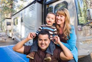 feliz joven familia de raza mixta frente a su hermosa rv en el campamento. foto