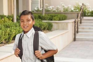 niño hispano feliz con mochila caminando en el campus de la escuela foto