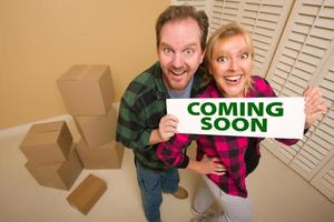 Goofy Couple Holding Coming Soon Sign in Room with Boxes photo