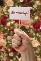 Hand Holding Ba Humbug Card In Front of Decorated Christmas Tree. photo