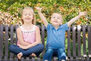 hermana joven y hermano divirtiéndose en el banco en el parque foto