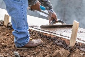 trabajador de la construcción usando paleta de madera en cemento húmedo formando para hacer frente a la nueva piscina foto